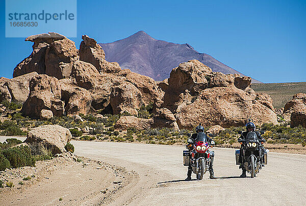 Zwei Freunde fahren auf einem Tourenmotorrad auf einer staubigen Straße in Bolivien