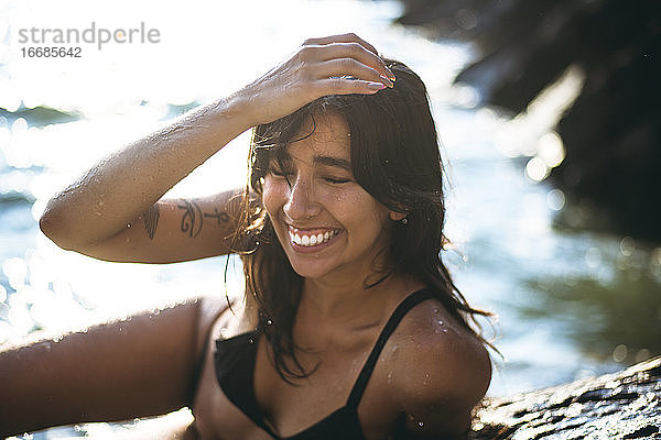Junge Latina Frau lachend am Meer zur goldenen Stunde im Sommer