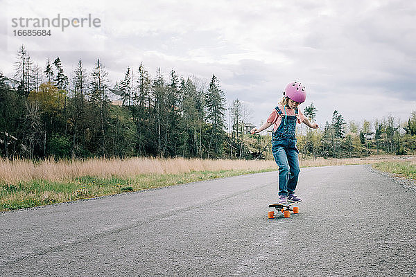 junges Mädchen lernt auf einer Landstraße Skateboard fahren