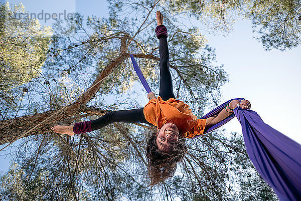 Junges Mädchen  Akrobatin. Übt Seiltanz in der Luft. Frau macht Zirkuskunststücke mit Kleidung im Wald. Straddle Fall Position.