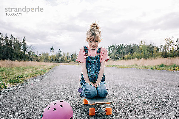 Porträt eines jungen Mädchens  das auf einem Skateboard sitzt und lächelt