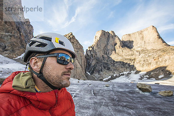 Porträt eines Bergsteigers mit Helm und Sonnenbrille unter einem Berggipfel