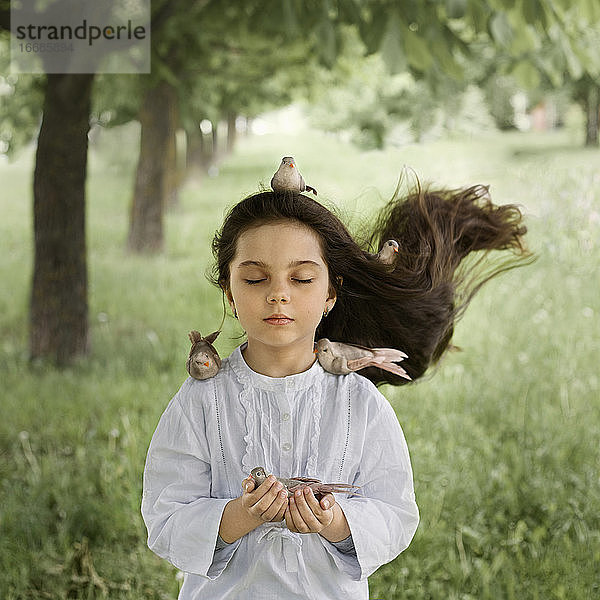 ein Mädchen mit offenem Haar und Vögeln  die auf ihr und in ihrem Haar sitzen