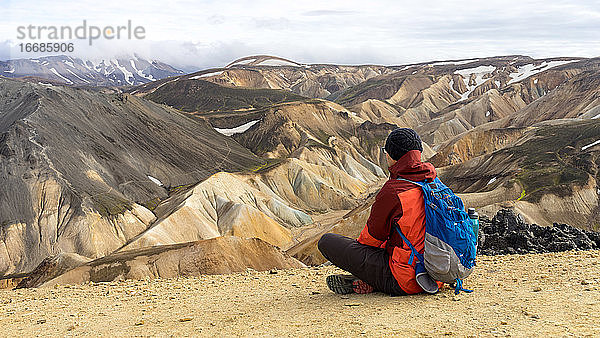 Männlicher Wanderer macht eine Pause mit Blick auf die Sandhügel von Landmannalaugar