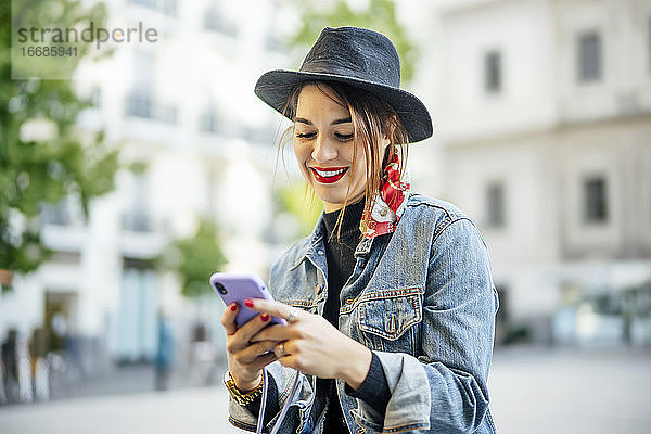 Schöne Frau im Herbstkleid mit Hut  die ein Mobiltelefon benutzt