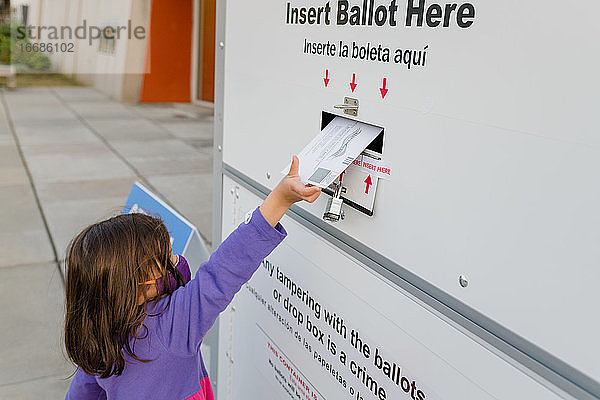 Kleines Mädchen wirft den Stimmzettel in einen Briefkasten für die Briefwahl