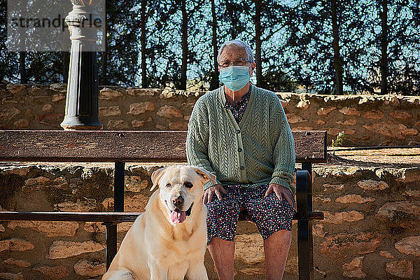 Großmutter mit ihrem Haustier sitzt auf einer Bank und hat eine Maske auf.