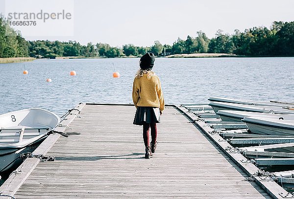 junges Mädchen  das entlang eines Piers in Richtung Meer in Schweden geht
