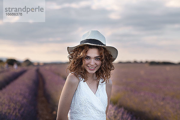 Frau mit lockigem Haar und Hut in einem Lavendelfeld