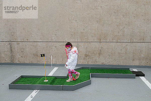 Mädchen in rosa Arztkostüm und Gesichtsmaske spielt Minigolf