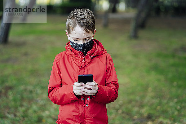 Junge in roter Jacke spielt mit seinem Smartphone