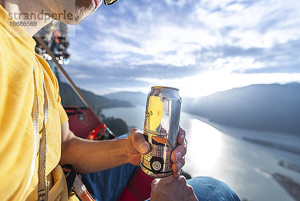 Mann trinkt und hält Bierdose bei Sonnenuntergang auf einem Portaledge Squamish