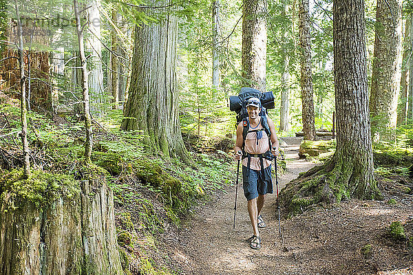 Ein lächelnder Rucksacktourist wandert auf einem Pfad durch einen alten Wald in Kanada.