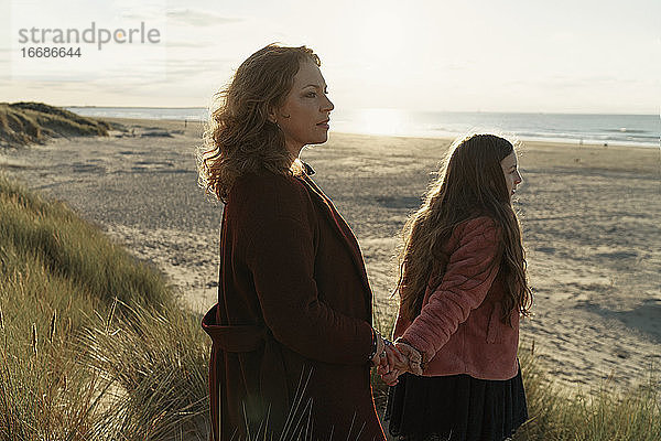 Mutter und Tochter am Strand stehend mit Blick aufs Meer