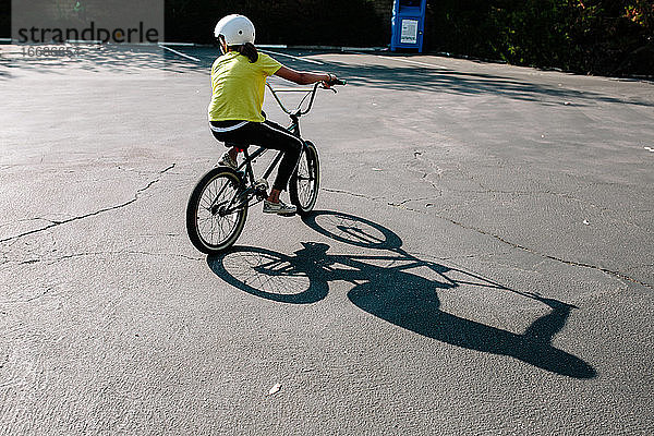 Rückansicht eines Mädchens und ihres Schattens beim Fahren eines BMX-Rads auf einem Parkplatz