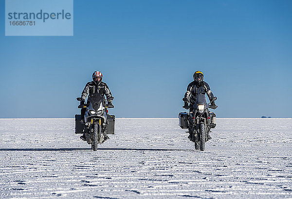 Zwei Männer fahren mit dem Motorrad über die Salinen von Uyuni