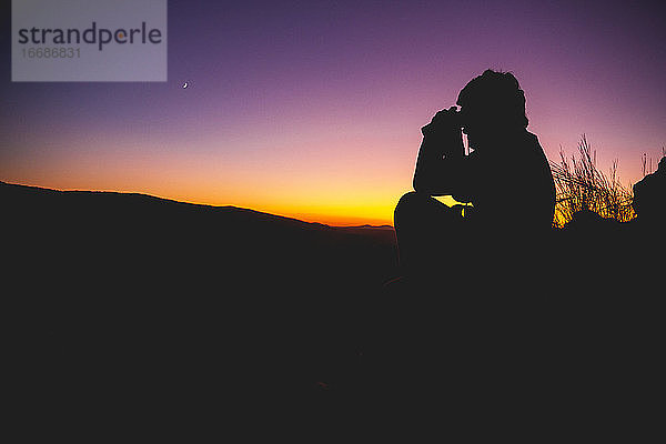 Silhouette eines Mannes mit Fernglas bei Sonnenuntergang mit dem Muh