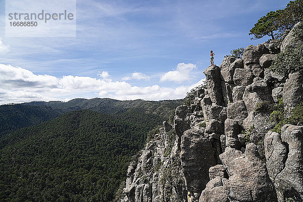 Eine Frau steht auf einer hohen Felsformation und beobachtet die Landschaft