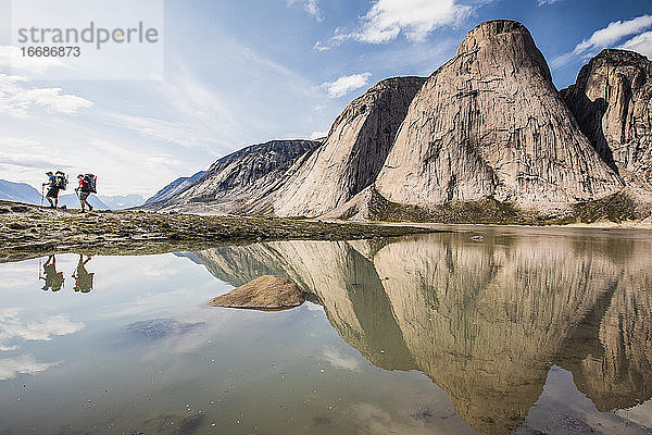 Reflexion von zwei Rucksacktouristen beim Wandern unterhalb steiler Berge