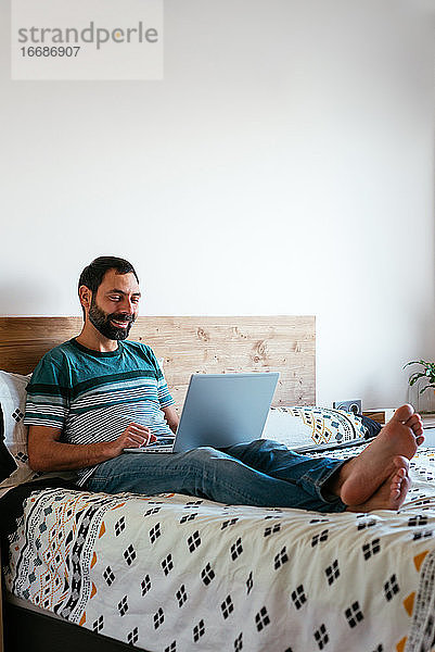 Junger Mann liegt auf dem Bett und führt einen Videoanruf