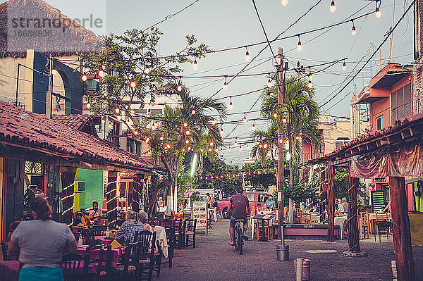 Mann auf Fahrrad in kleiner Stadt in Mexiko mit Restaurants am Abend