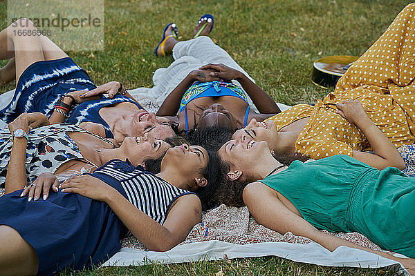 Gruppe von lächelnden Freundinnen  die auf einem Handtuch in einem Park liegen und Spaß haben