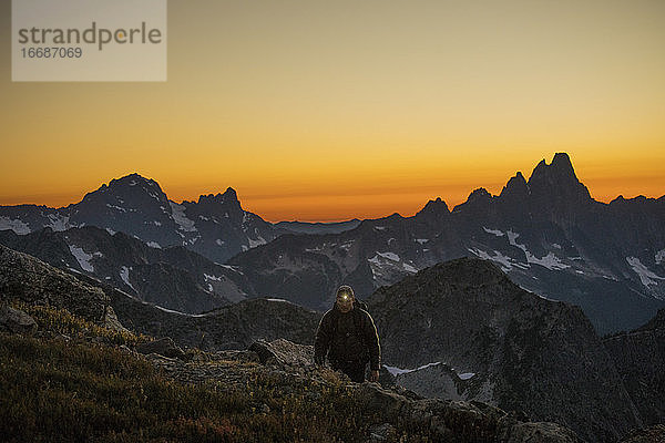 Wanderer wandert mit Stirnlampe auf einem Bergkamm nach Sonnenuntergang.