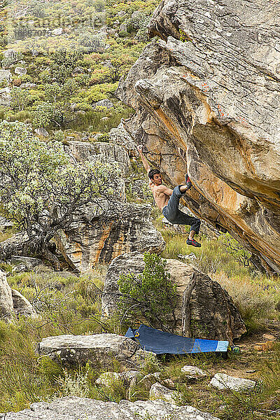 Sportlicher Mann klettert draußen auf einen Felsbrocken über Crashpads