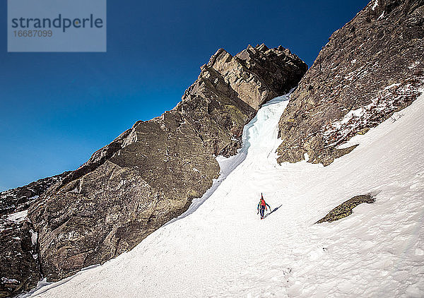 Eiskletterer geht mit Skiern auf dem Rücken auf eine Eisrinne zu