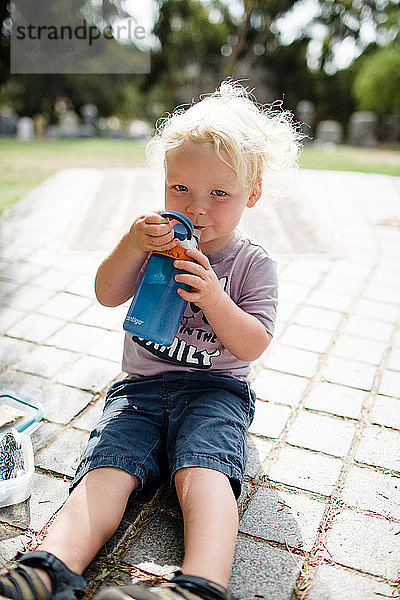 Zweijähriges Kind  das beim Trinken von Wasser in die Kamera grinst