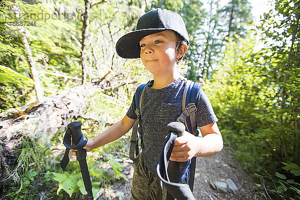 Junger Junge beim Wandern mit Trekkingstöcken  der einen Rucksack trägt.