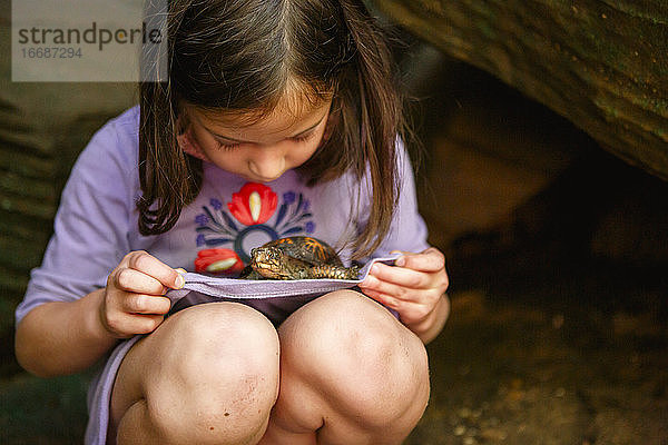 Ein kleines Mädchen mit schmutzigen Knien hält eine kleine Schildkröte auf dem Schoß