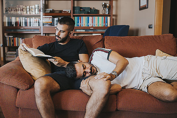 Junge liegt auf seinem Freund  während er auf dem Sofa ein Buch liest