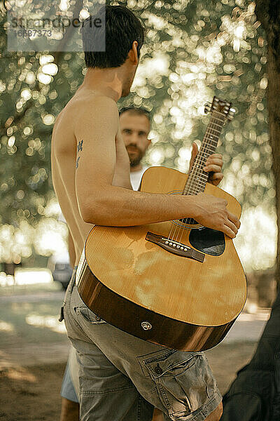 Nahaufnahme eines barbusigen Mannes  der draußen Akustikgitarre spielt