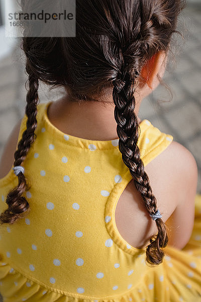 Kleines Mädchen mit Zöpfen im gelben Kleid