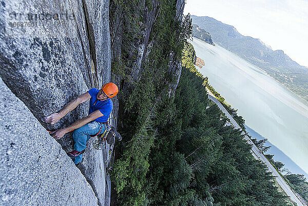 Mann klettert im Vorstieg auf Granit in Squamish mit Blick auf den Ozean im Hintergrund