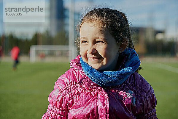 Lächelndes kleines Mädchen in einem rosa Mantel in einem Fußballstadion