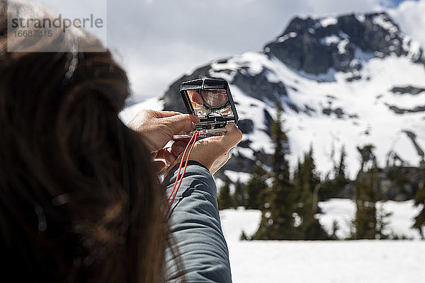 Unerkennbare Wanderin  die einen Kompass zur Navigation während einer Tour durch verschneite Berge an einem bewölkten Tag benutzt