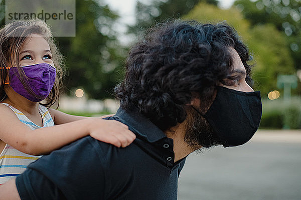 kleines Mädchen reitet Huckepack mit ihrem Vater und trägt Gesichtsmasken