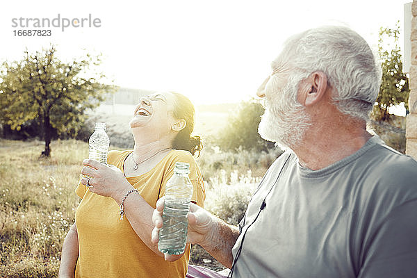Ein älteres Paar lacht  während es sich ausruht  um Wasser zu trinken