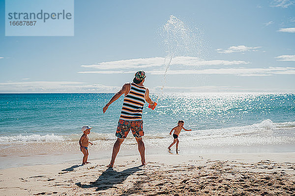 Kinder  die mit ihrem Vater an einem sonnigen Tag am Strand mit Wasser spielen