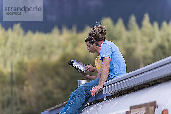 zwei Personen sitzen auf dem Dach eines Schulbusses und lesen einen Kletterführer