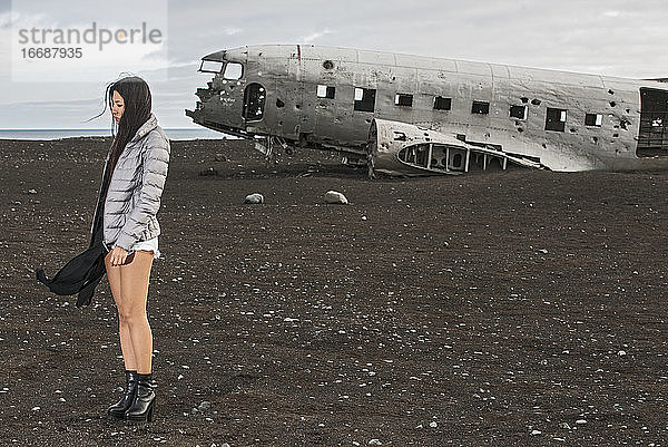 schöne Frau posiert vor einem verlassenen Flugzeugwrack in Island