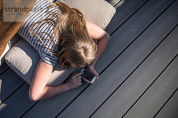 Junges Mädchen mit Smartphone an Deck liegend