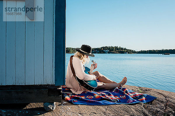 Frau saß friedlich Gitarre spielend am Strand an einem sonnigen Tag