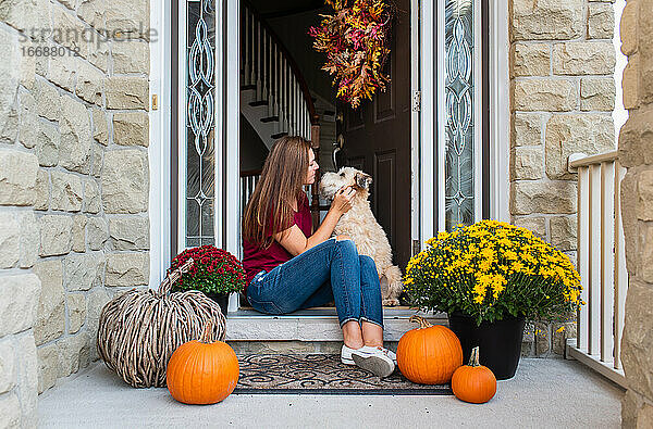 Frau und ihr Hund sitzen in der Tür eines herbstlich dekorierten Hauses.