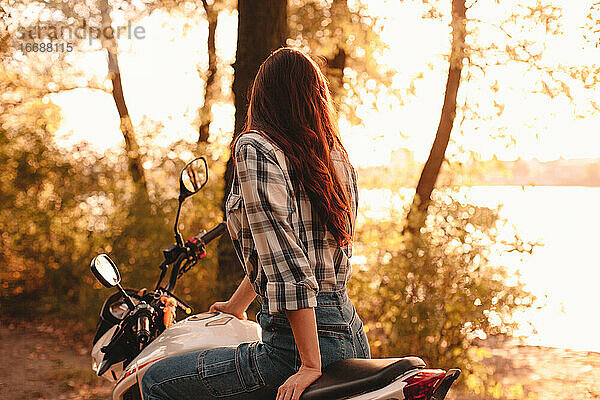 Frau betrachtet die Aussicht  während sie auf einem Motorrad sitzt und sich am Fluss entspannt