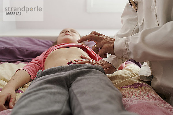 Ärztin  die den Unterleib eines kleinen Mädchens in ihrem Zimmer untersucht. Hausarzt-Konzept