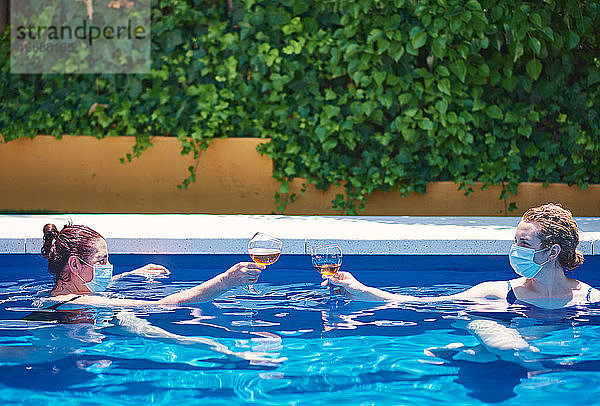 Zwei Frauen stoßen in einem Pool an. Sie tragen Masken  um die Ausbreitung des Virus zu verhindern.