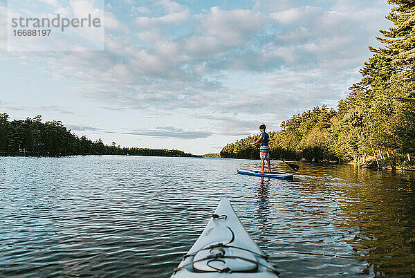 Ein Jugendlicher paddelt auf einem SUP auf einem See in Ontario  Kanada  mit einem Kajakfahrer.